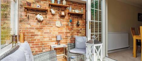 A cozy room with wicker furniture, a brick wall, and shelves with decorative items.