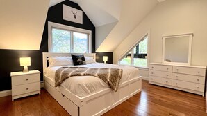 A bedroom with a large bed, two bedside tables, a dresser, a mirror, and a window with a view of trees. - Gavia Chalet - Mountain Views - Private Hot Tub - Loon Mtn - Kancamangus Highway (Lincoln)