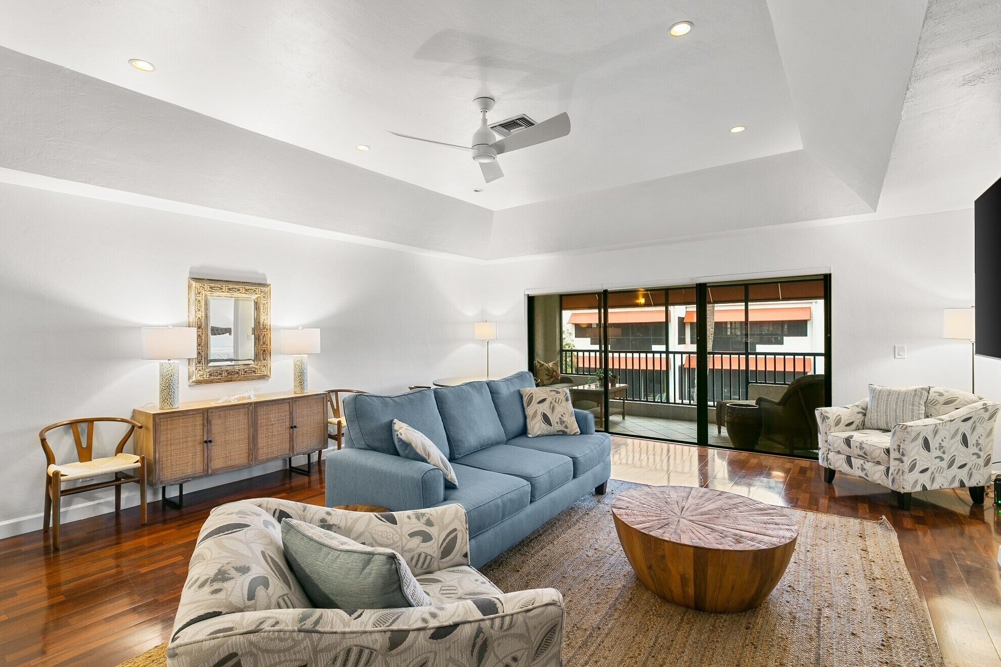 A spacious living room with a blue sofa, patterned armchairs, a wooden coffee table, and a ceiling fan.