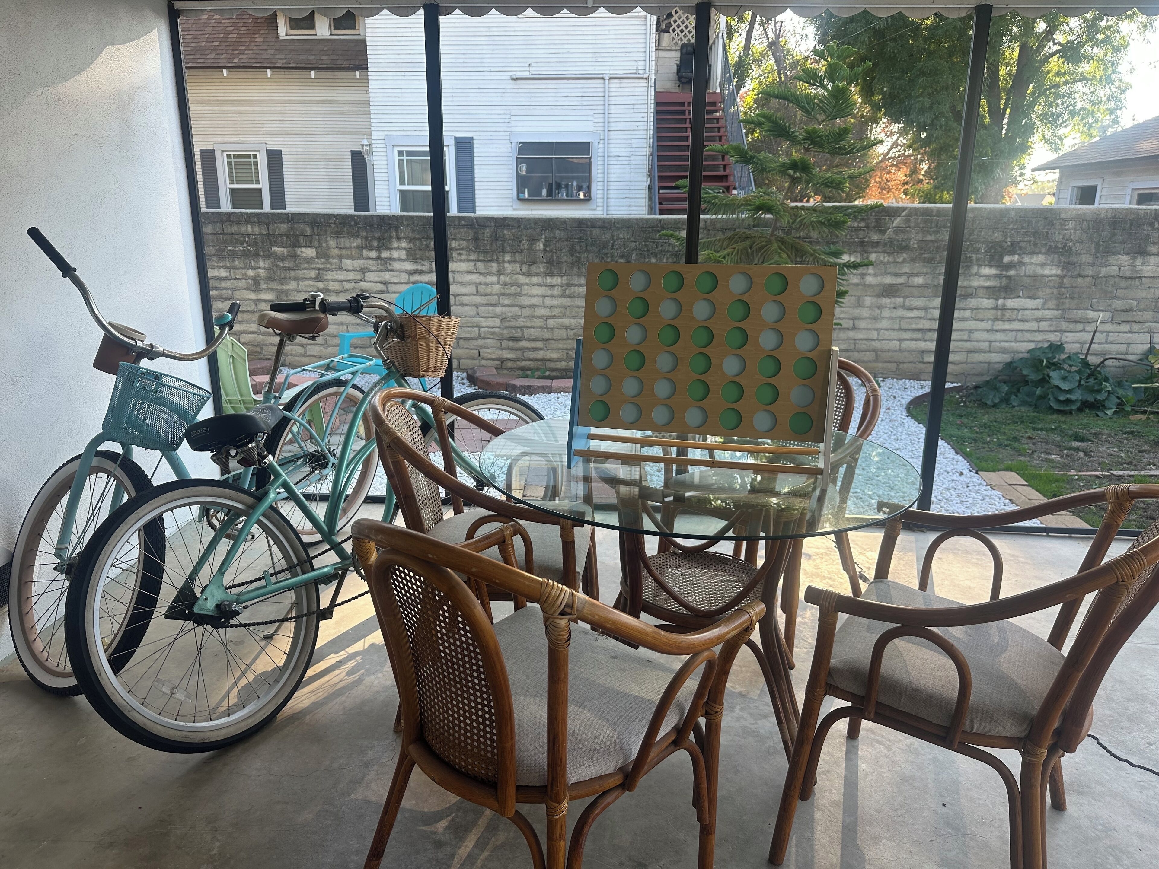 Un patio con sillas de mimbre, una mesa de vidrio, una bicicleta y vistas a una calle residencial.