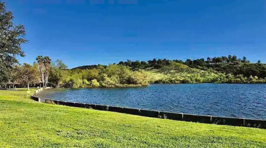 Eine grüne Fläche mit einem Gewässer und einer hügeligen Landschaft im Hintergrund.