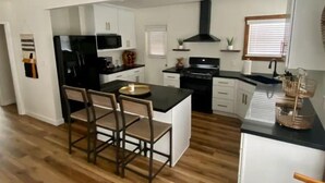 A modern kitchen with a central island, bar stools, white cabinetry, and a black stove.