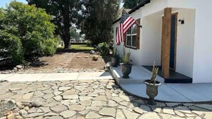 A white building with a stone pathway leading to the entrance. There are potted plants and an American flag on the building.