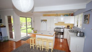 Une cuisine moderne avec des meubles blancs, un îlot central doté de tabourets, une grande fenêtre et une vue sur l’extérieur.