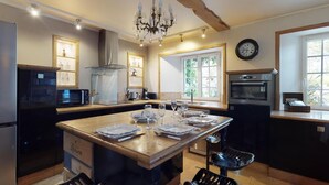 Une cuisine dotée d’un îlot central, d’un lustre, d’une horloge et d’une fenêtre offrant une belle vue.