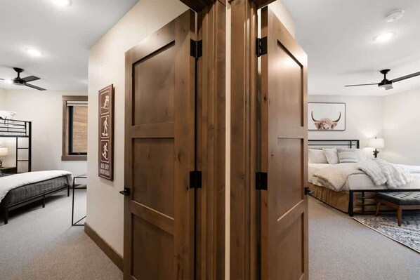 Ein Schlafzimmer mit einer großen Holztür, einem Bett mit weißer Bettdecke, einem Nachttisch und einem Deckenventilator.