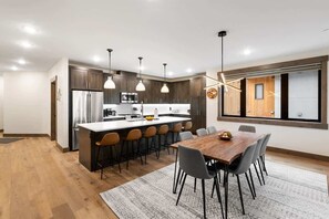 Eine moderne Küche mit einer zentralen Kochinsel, Pendelleuchten und einem Essbereich mit Holztisch und Stühlen.