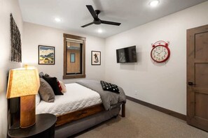 Ein Schlafzimmer mit Bett, Deckenventilator, Wand-Fernseher, rotem Wecker und Holztür.