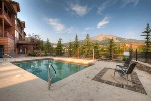A pool area with a view of mountains, a wooden building, and a fenced garden.