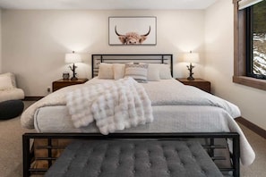 A bedroom with a bed, bedside tables, a bench, a framed picture on the wall, and a window.