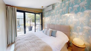 Quarto com uma cama grande, ventilador de teto, vista para o exterior e parede com padrão de água-viva.