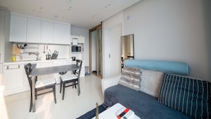 A modern kitchen with white cabinets, a dining table, and chairs. There is a sofa with a blue cushion and striped pillows.