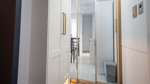 A hallway with a glass door leading to a room, a small trash bin, and a visible chair in the background.