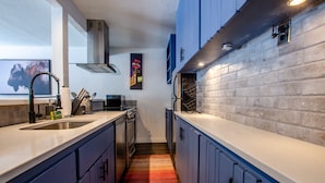 Cocina estrecha con alfombra a rayas, electrodomésticos de acero inoxidable y gabinetes azules.