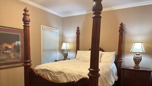Un lit à baldaquin avec une couvre-lit beige, deux tables de chevet avec des lampes, une fenêtre avec des stores et un tableau à motifs léopard accroché au mur.