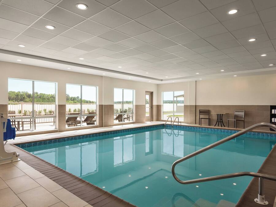 An indoor swimming pool with clear glass walls, a tiled floor, and a metal pool ladder.