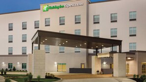 Edificio de Holiday Inn Express & Suites con entrada cubierta, múltiples ventanas y un área ajardinada con plantas pequeñas.