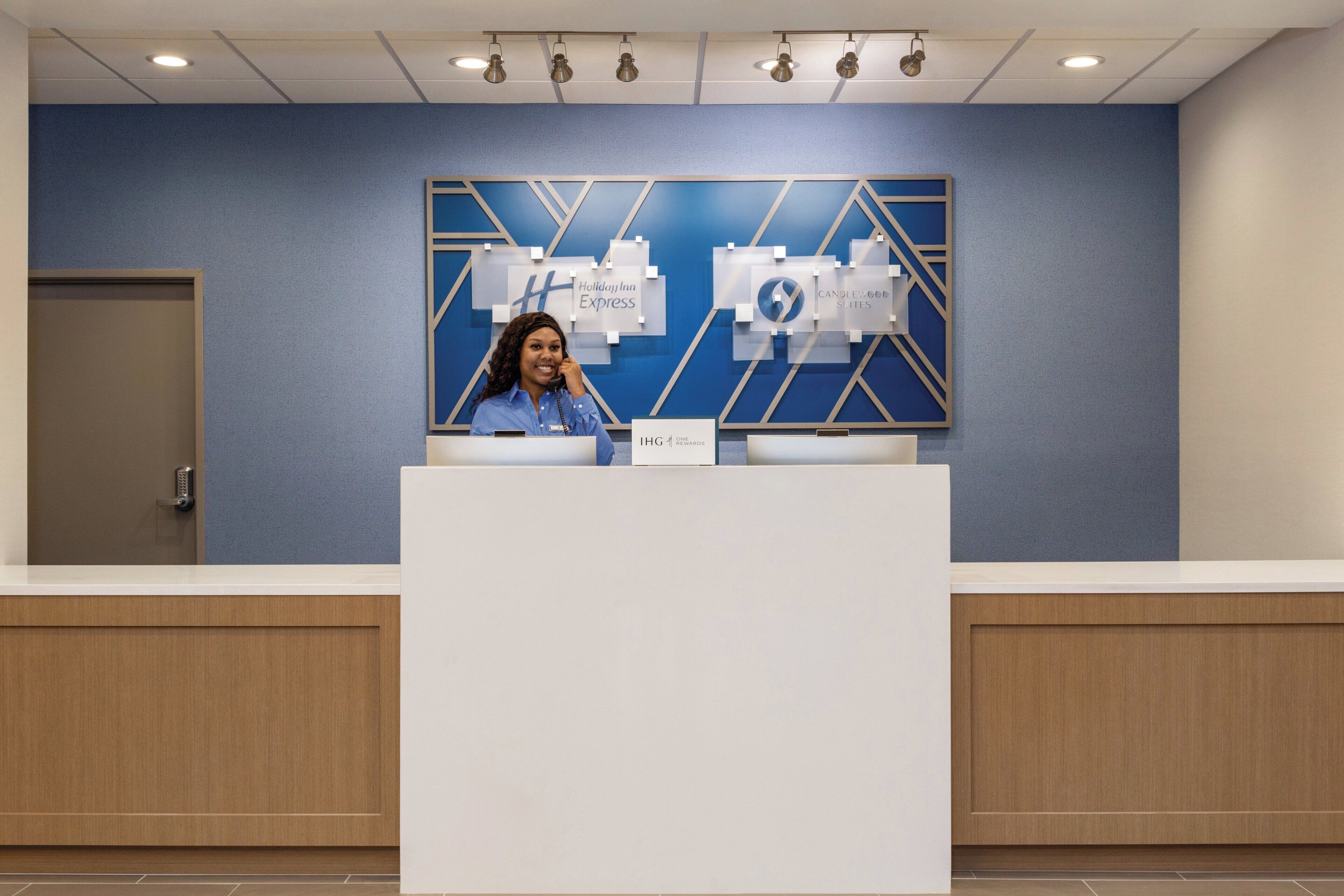Een receptiebalie met een blauwe muur en een geometrisch ontwerp, een bord met Holiday Inn Express, en een gesloten deur links.