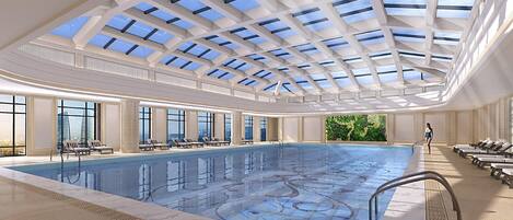 A large indoor swimming pool with a skylight ceiling, sun loungers, and a view of the city.
