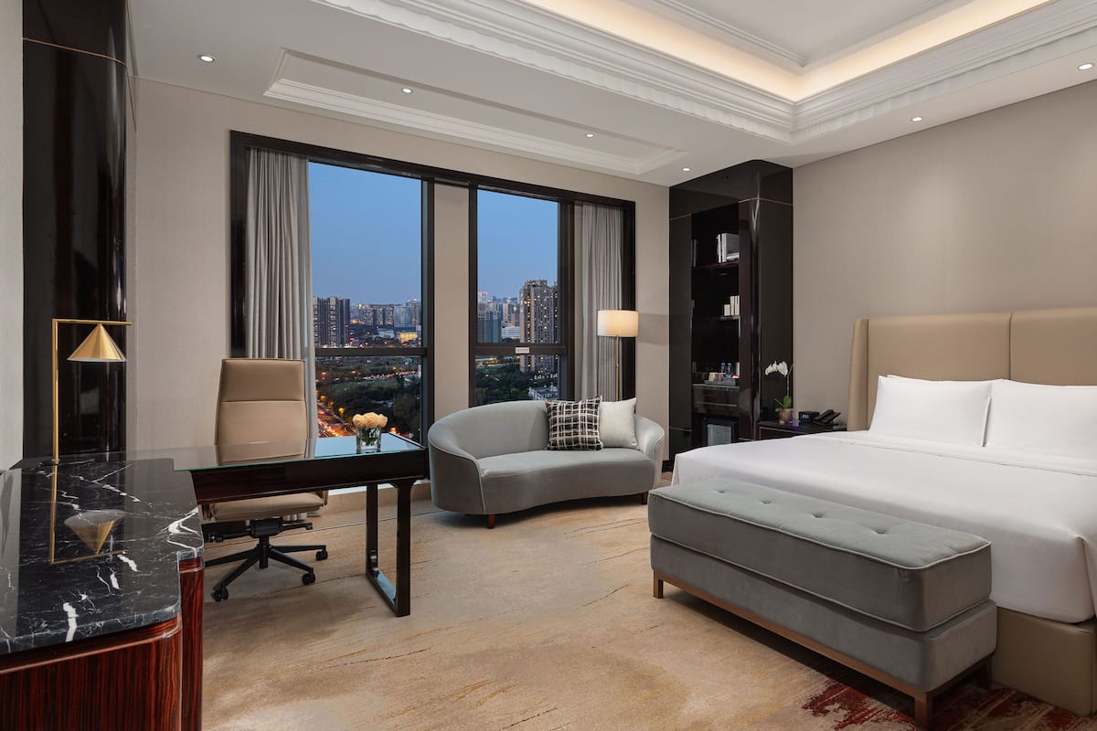 Ein Hotelzimmer mit Bett, Schreibtisch, Stuhl und Blick auf die Stadtlandschaft.