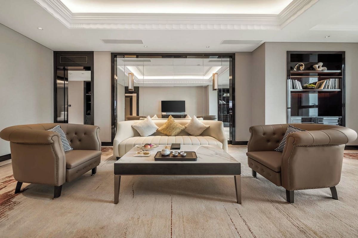 Ein modernes Wohnzimmer mit einer Couch, zwei Sesseln, einem Couchtisch und einem Bücherregal.