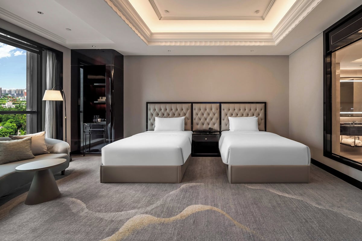 Ein Hotelzimmer mit zwei Betten, einem Schlafsofa, einem kleinen Tisch und Blick auf die Stadt.
