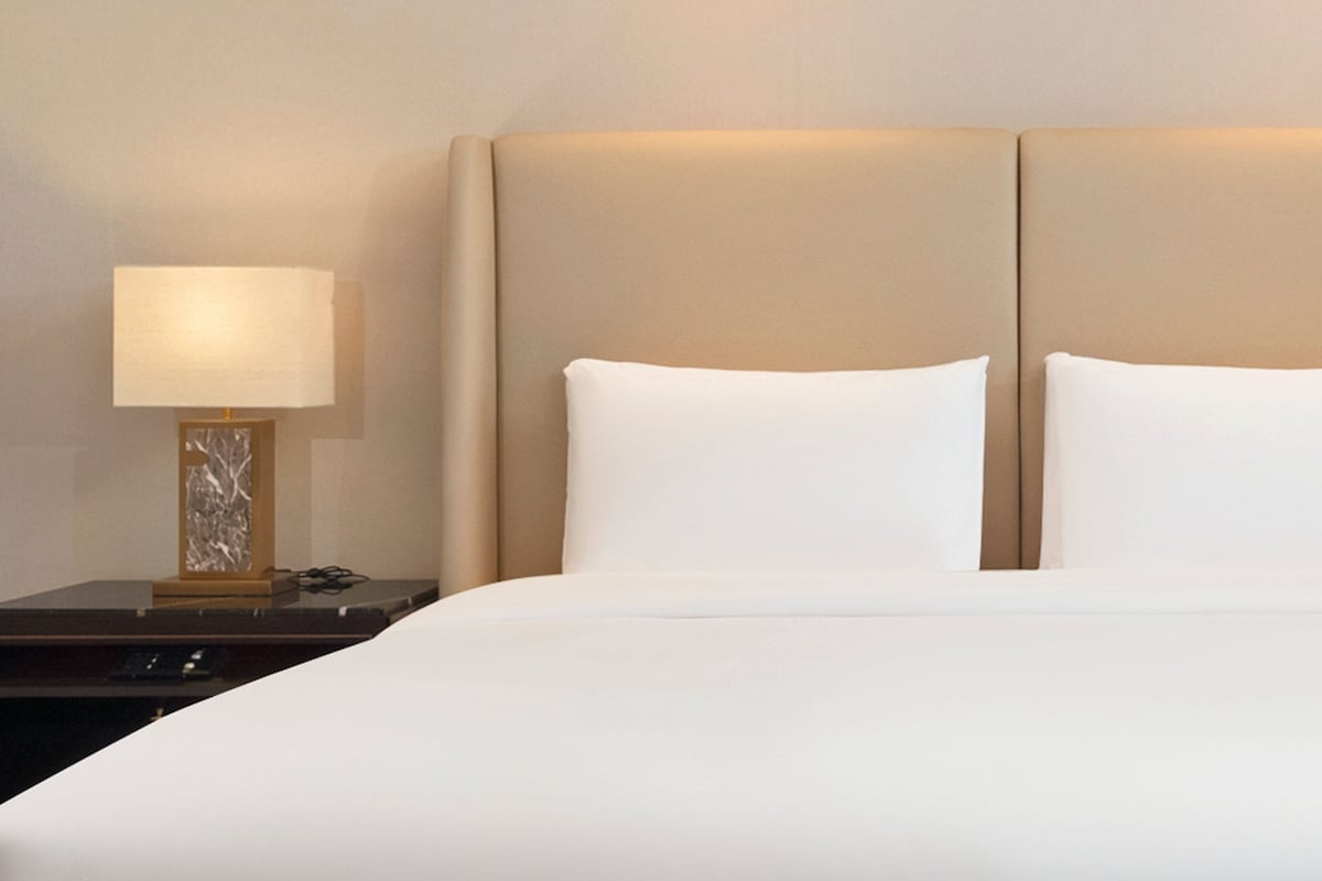 Une chambre d’hôtel avec un lit, deux oreillers, une table de chevet et une lampe.
