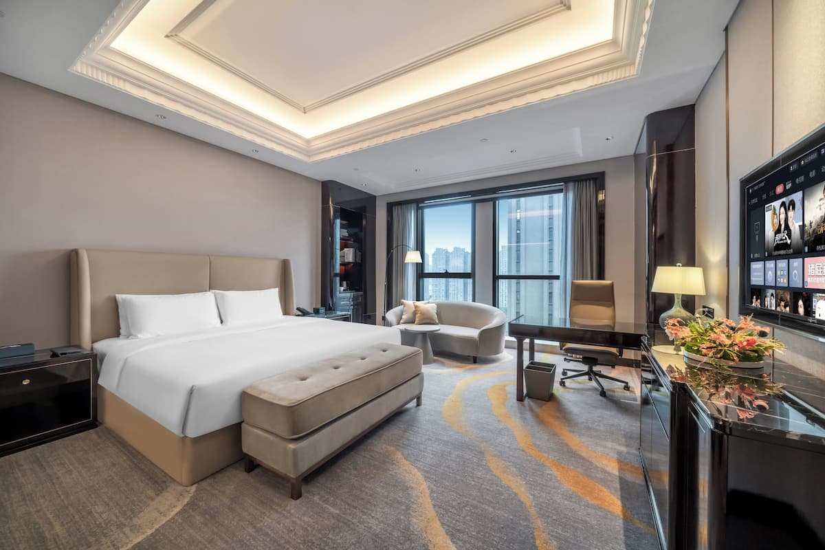Ein modernes Hotelzimmer mit einem großen Bett, einer Couch, einem Schreibtisch und einem Fernseher.