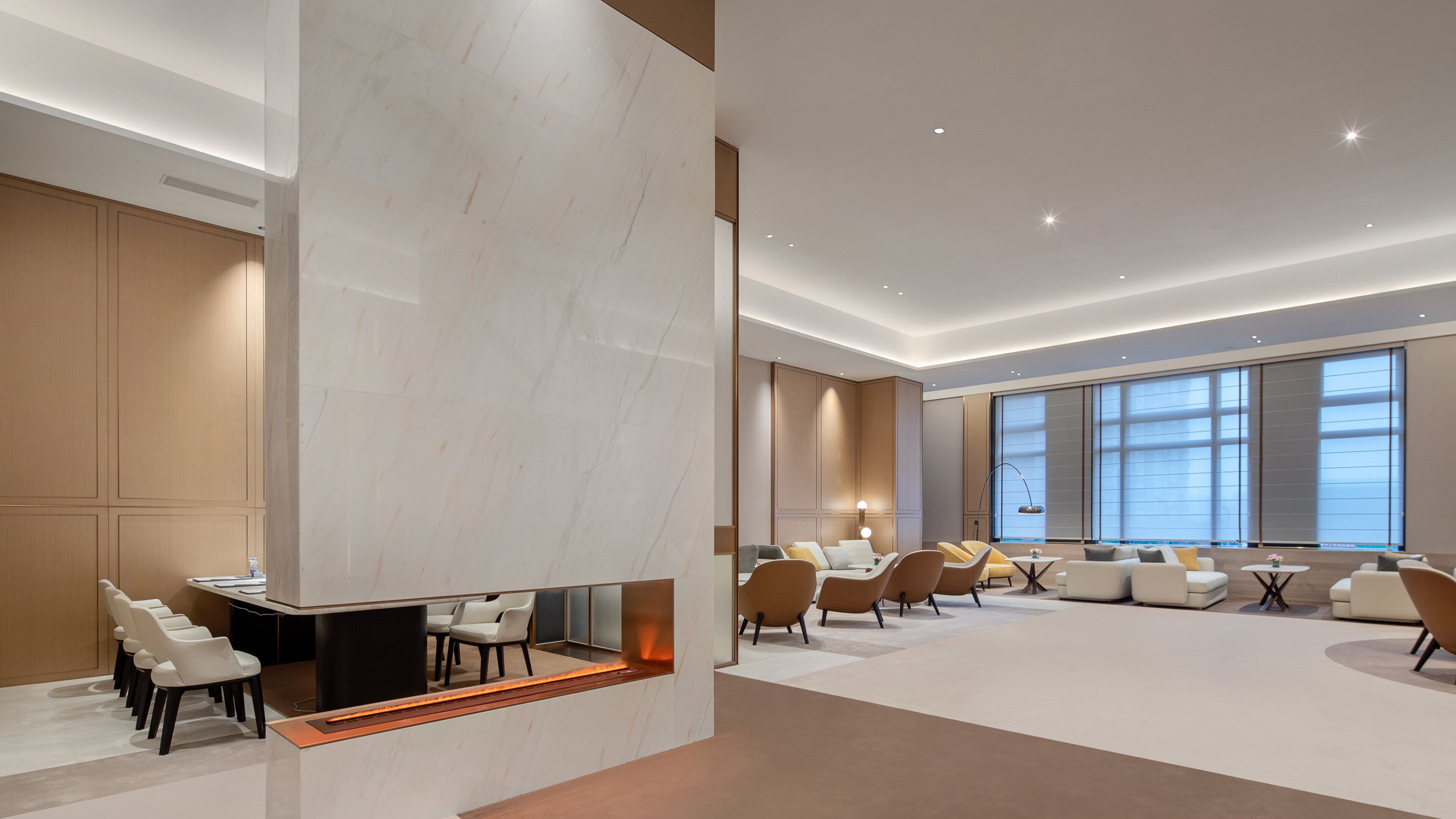 A modern hotel lobby with a central seating area, a fireplace, and large windows.