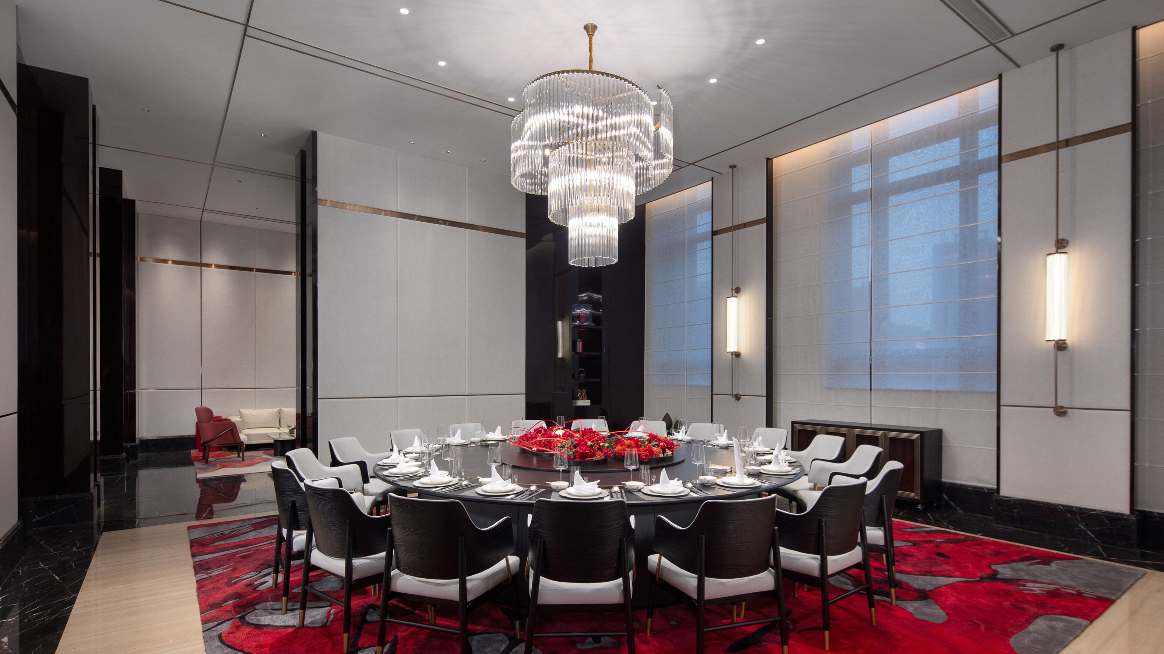 Ein moderner Konferenzraum mit rundem Tisch, schwarz-weißen Stühlen, einer Chandelierleuchtre und großen Fenstern.