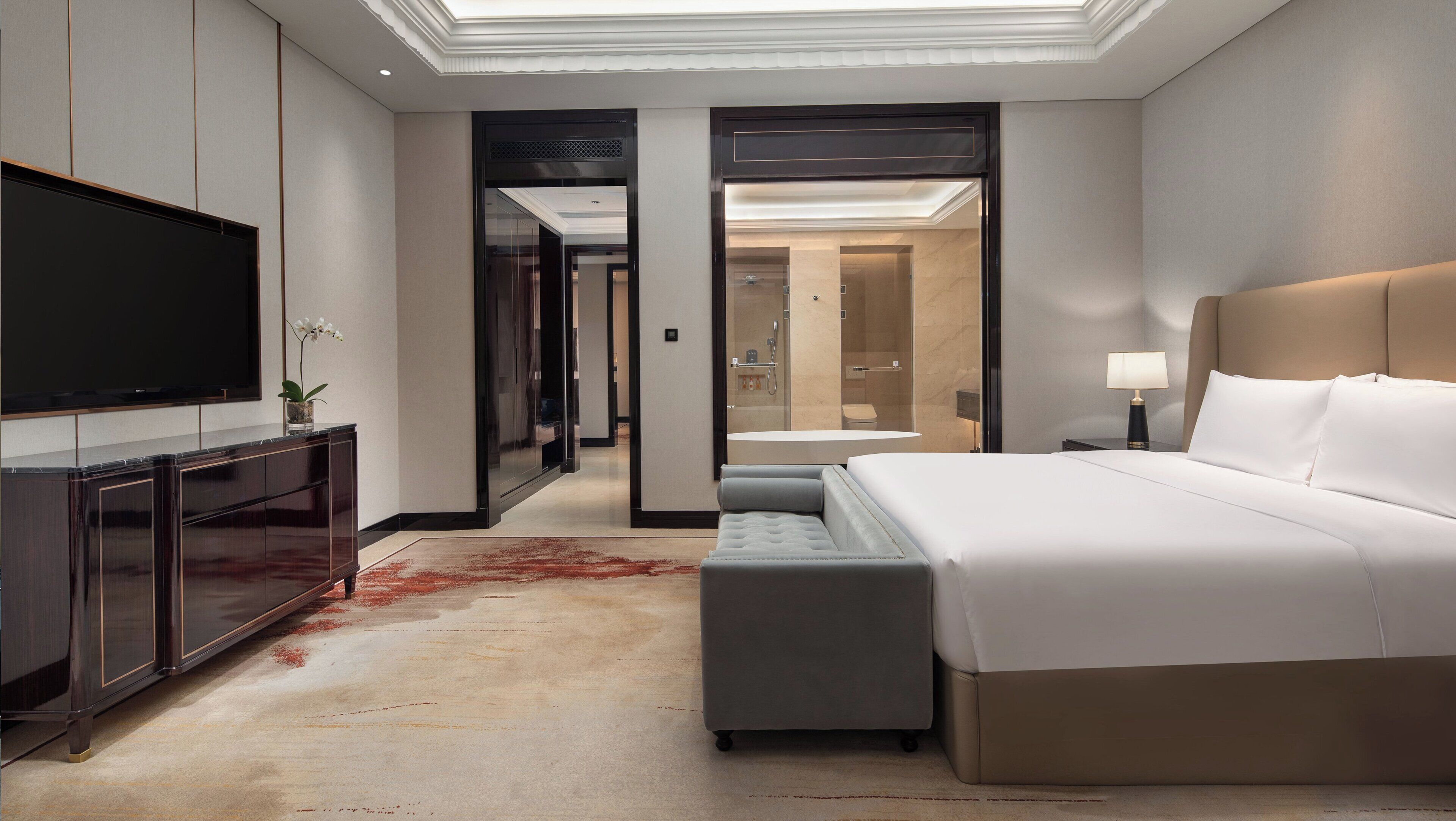 A modern hotel room with a large bed, a flat-screen TV, a desk, and a walk-in closet.