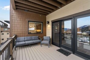 Ein Balkon mit einer Couch und Sesseln, einer Schiebeglastür und Blick auf die Berge.