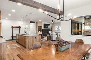 A modern kitchen with wooden cabinets, a central island, pendant lighting, and a dining area with a wooden table and chairs. - Ski-in/Ski-Out Slopeside Luxury Condo in Big Sky (Big Sky)
