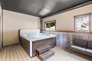 A modern outdoor hot tub area with a wooden deck, a built-in bench, and a view of a snowy landscape through a window. - Ski-in/Ski-Out Slopeside Luxury Condo in Big Sky (Big Sky)