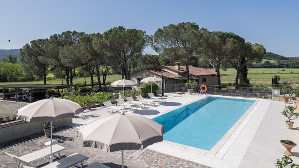 Ein Poolbereich mit Liegestühlen und Sonnenschirmen, umgeben von Bäumen und einem Haus im Hintergrund.