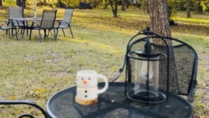 A round metal table with a mug and a glass pitcher, surrounded by chairs, in a park with autumn trees.
