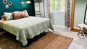 A bedroom with a bed, a rug, a chair, a mirror, and a window with curtains.