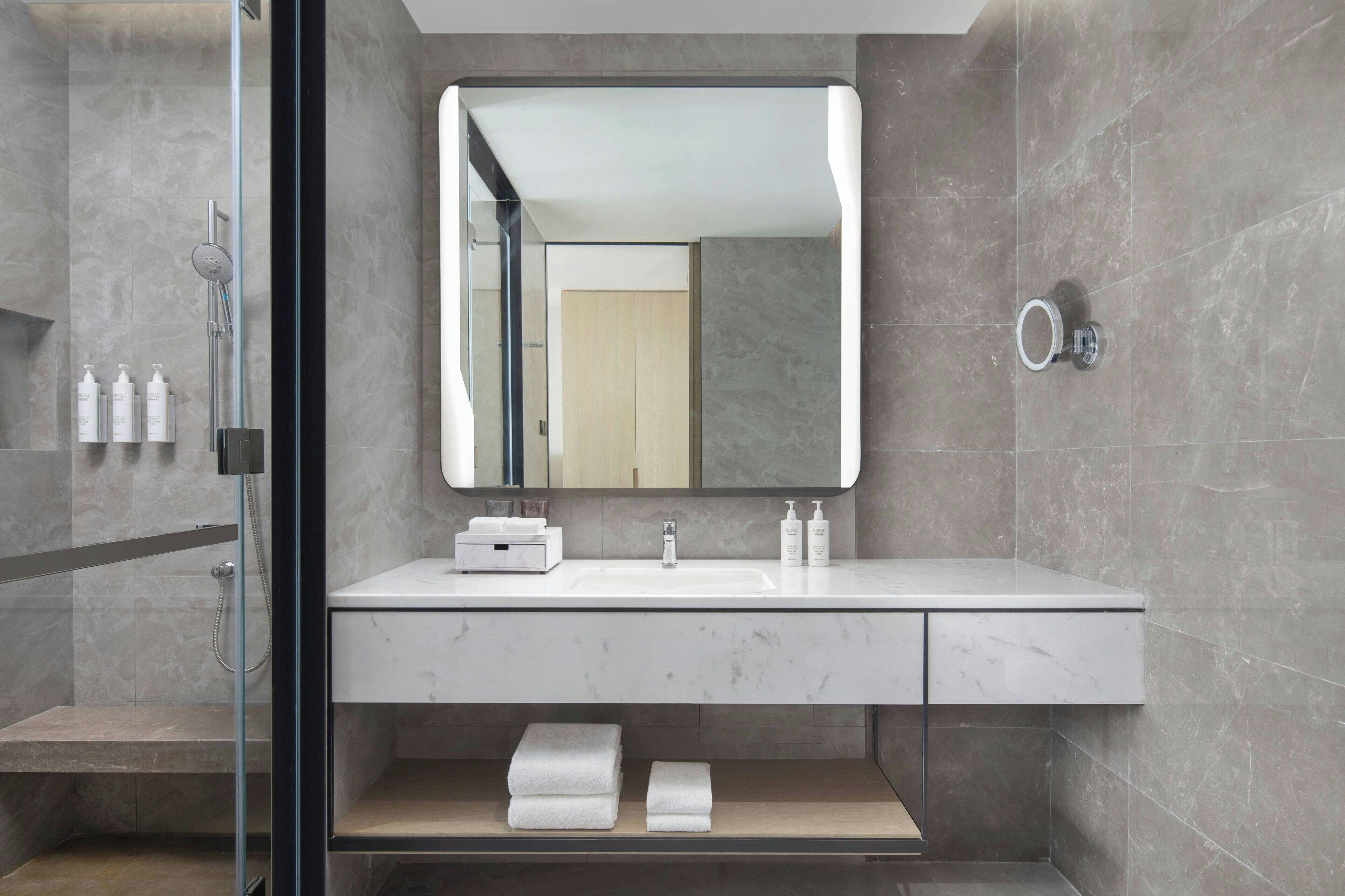 A modern bathroom with a glass shower enclosure, a white marble sink, and a large mirror.