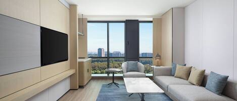 Una sala de estar moderna con un televisor grande, un sofá, una mesa de centro y vistas de la ciudad a través de amplios ventanales.