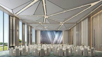 A spacious banquet hall with round tables and chairs, large windows, and a modern ceiling design.