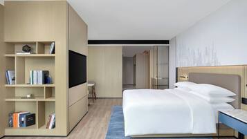A modern hotel room with a large bed, a built-in bookshelf, a flat-screen TV, and a small desk.