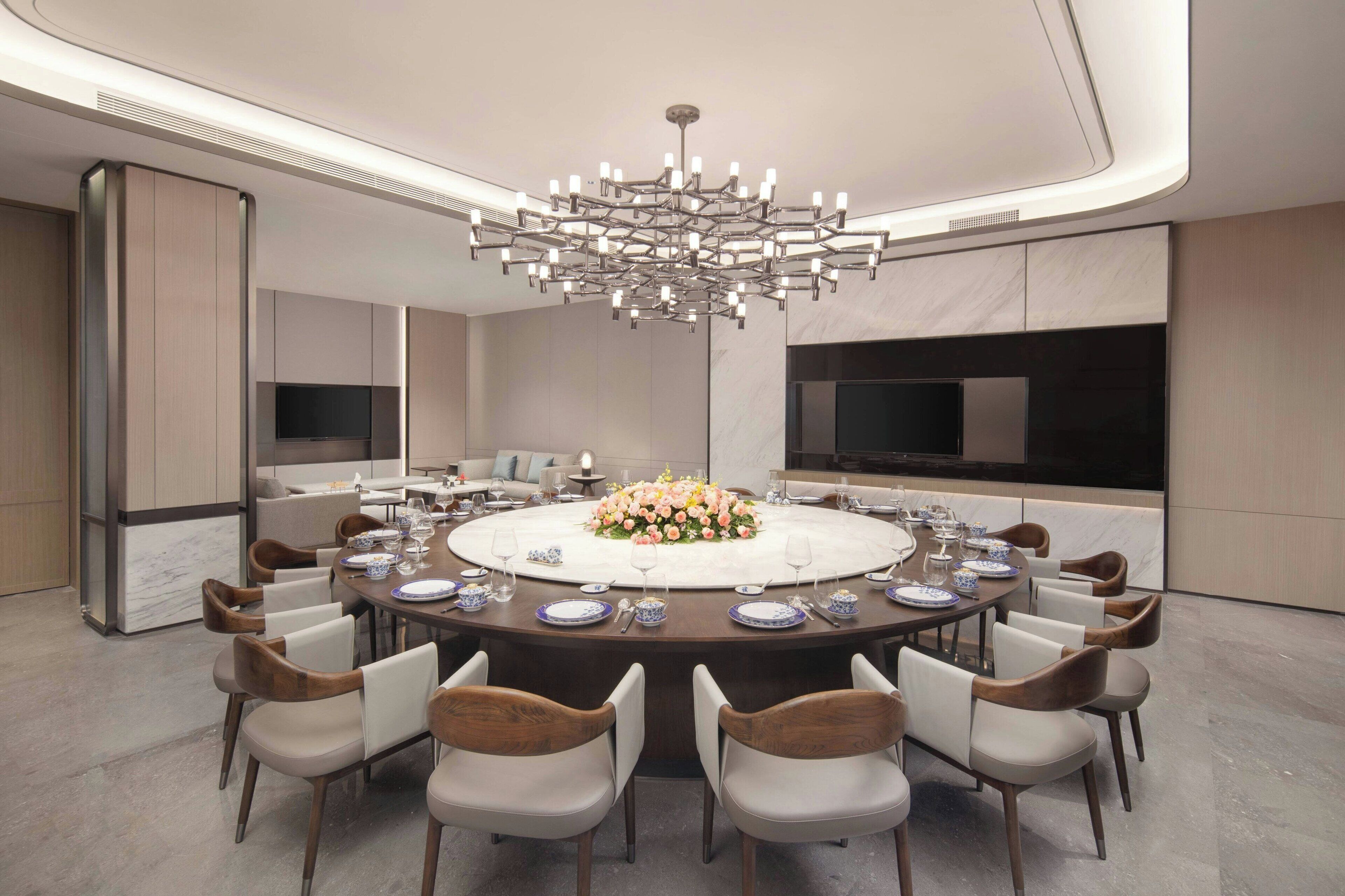 Un'elegante sala da pranzo moderna con un tavolo rotondo, sedie, un lampadario e una TV a parete.