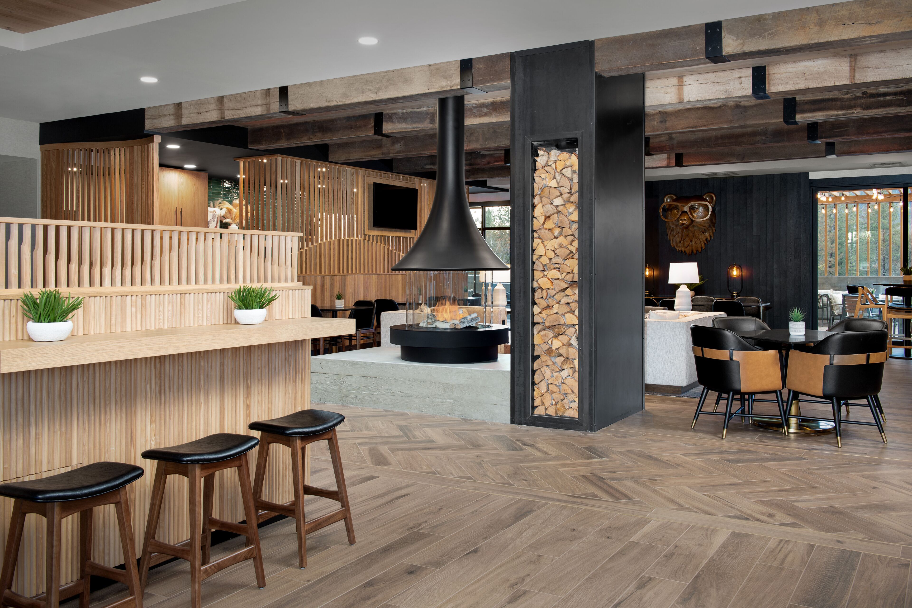 A modern bar area with wooden bar stools, a large pendant light, and a stone wall.