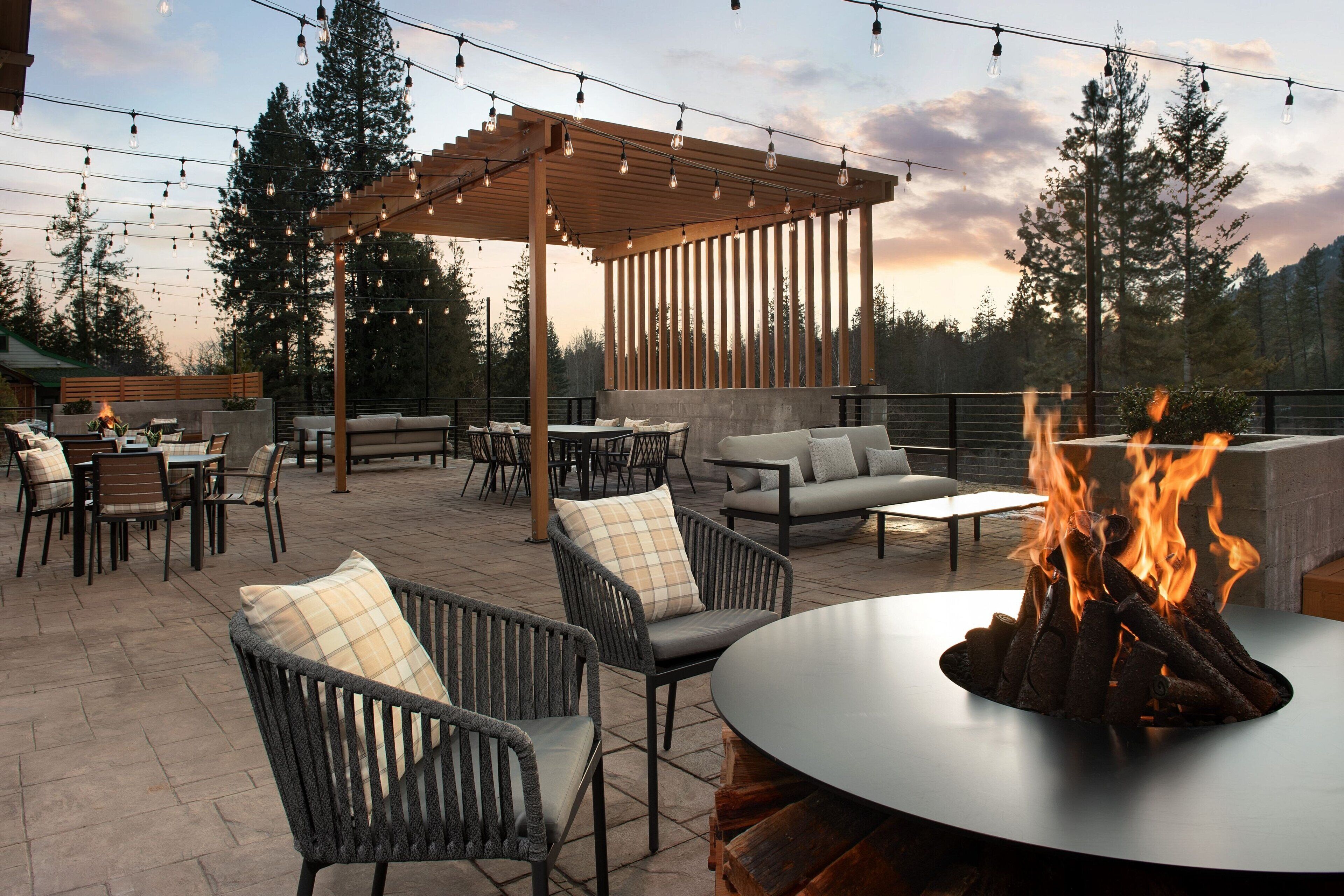 An outdoor patio with seating, a fire pit, and string lights.