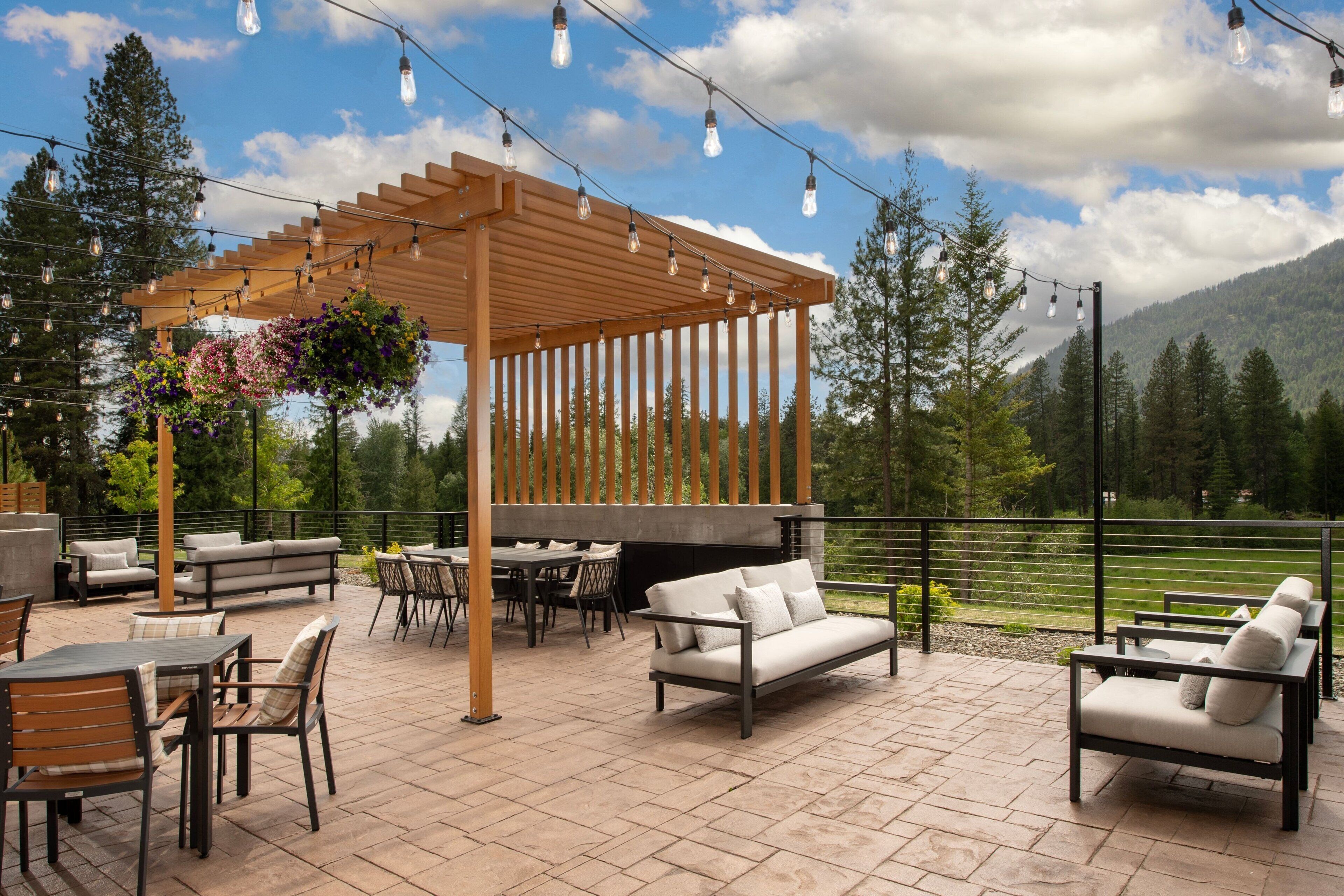 Een terras buiten met een pergola, zitplaatsen en lichtjes.