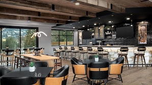 Ein modernes Restaurant mit Barbereich, Holzboden und großen Fenstern mit Blick ins Freie.
