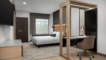 Een moderne hotelkamer met een bed, bureau, stoel en een grote spiegel.