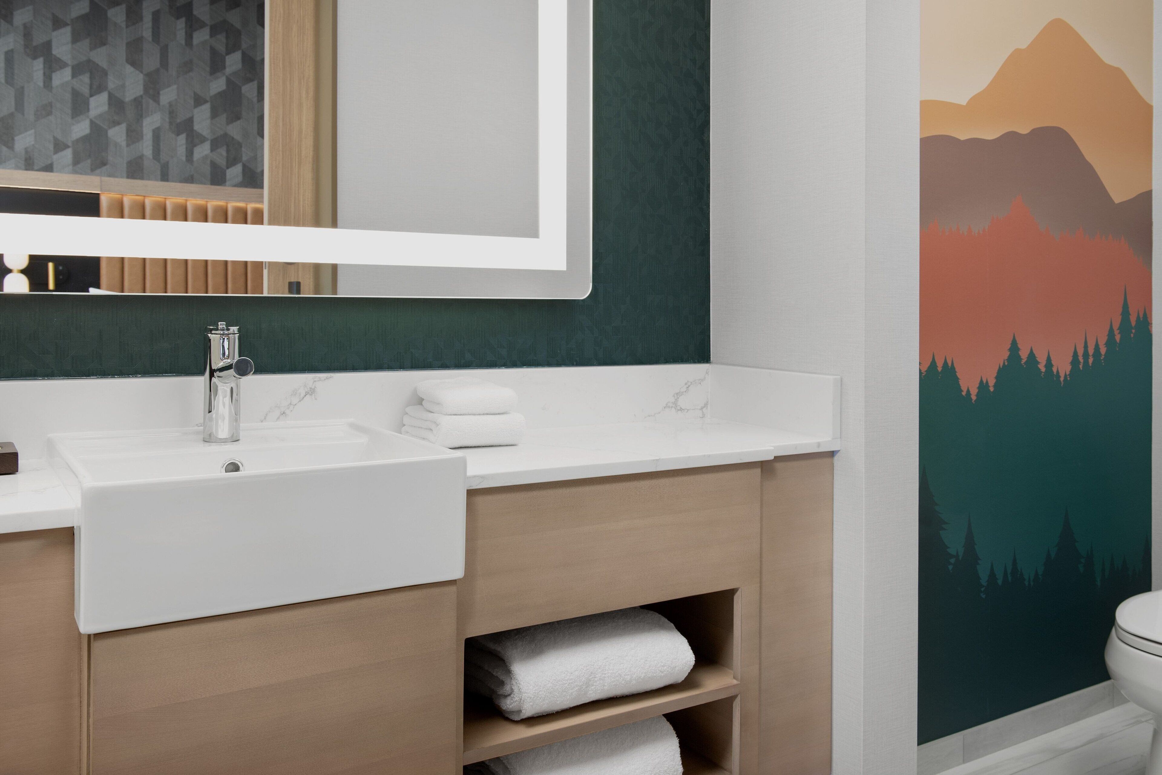 A modern bathroom with a white sink, wooden vanity, and a large mirror.