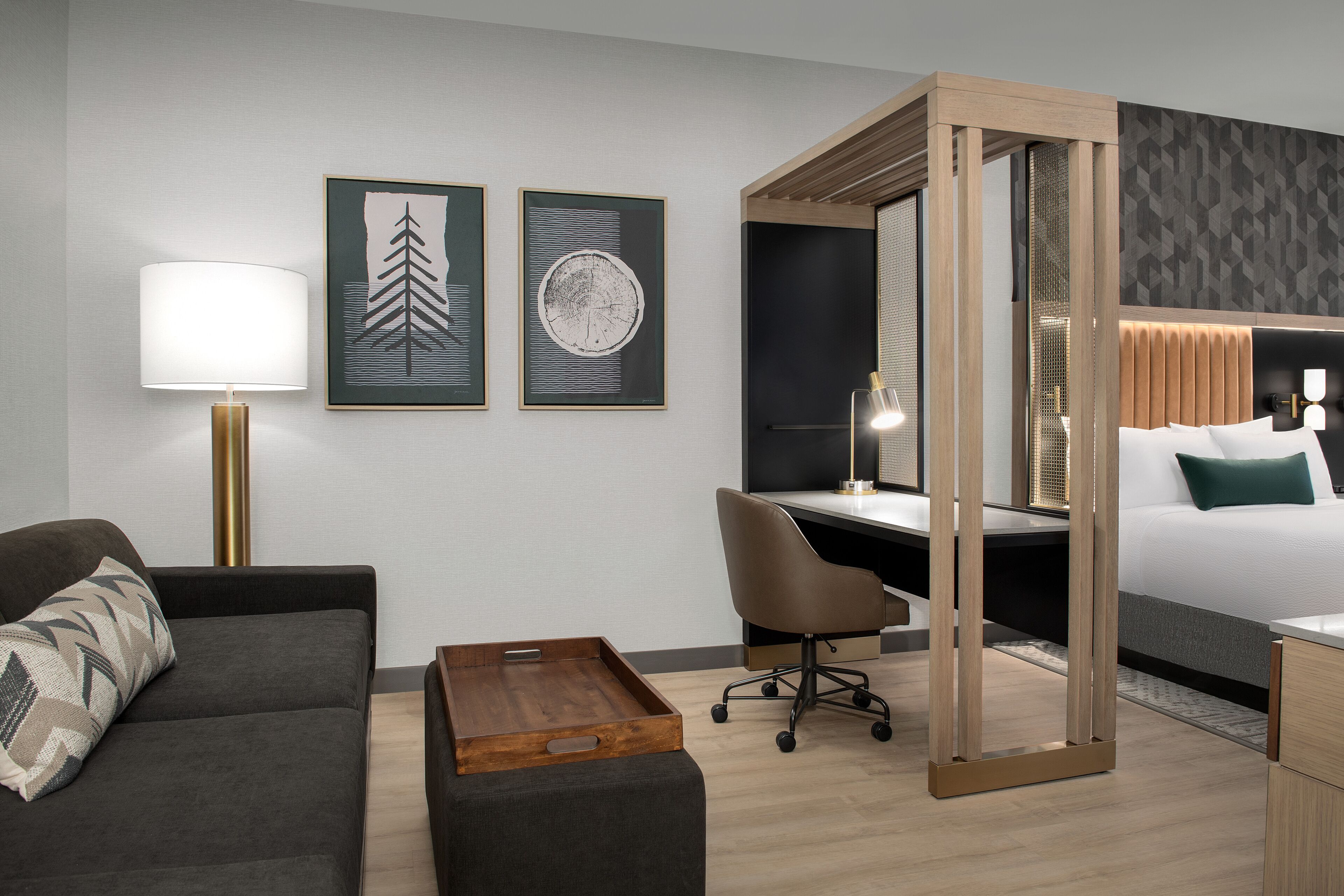 A modern hotel room with a sofa, a desk, a bed, and artwork on the wall.