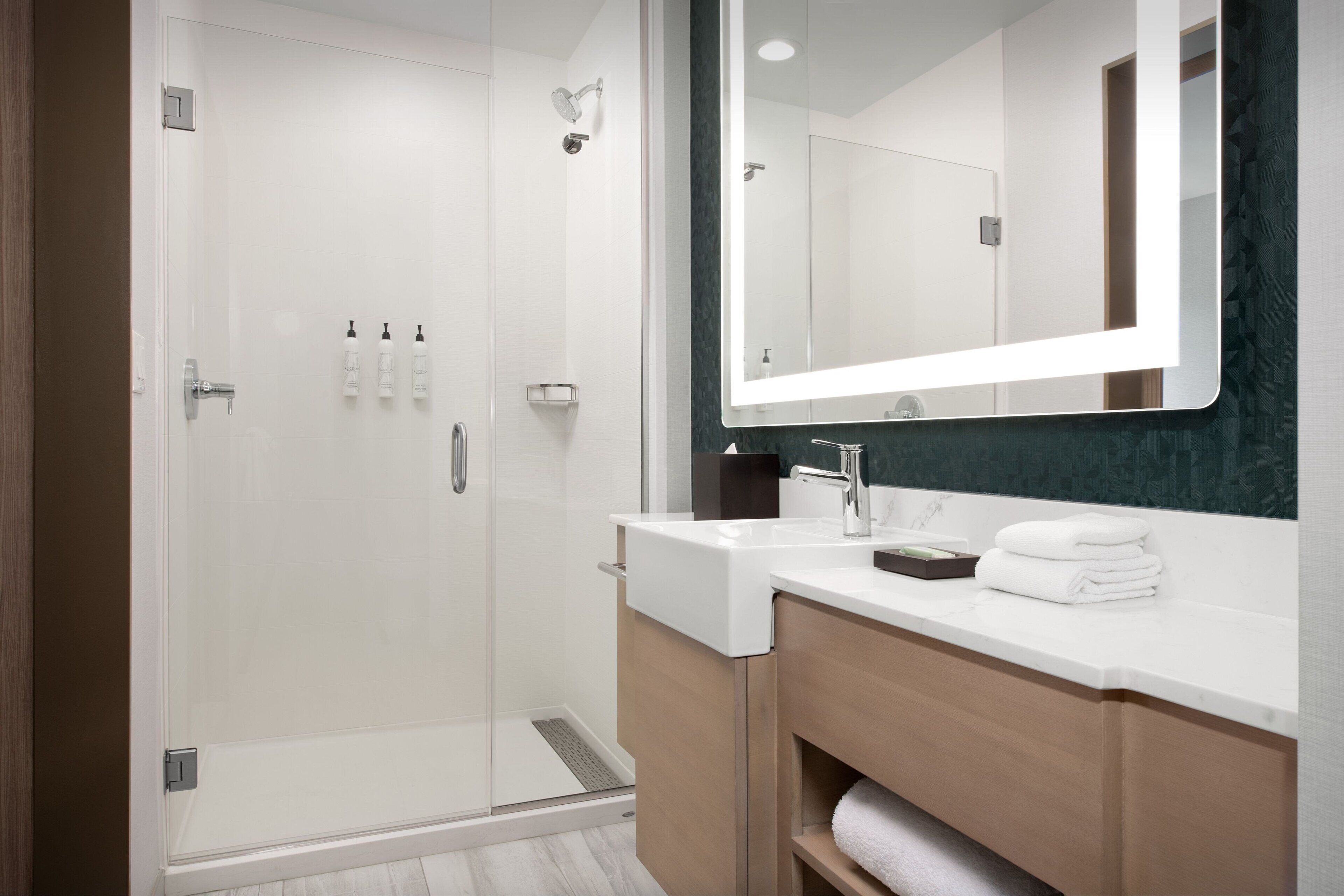 A modern bathroom with a glass-enclosed shower, a large mirror, and a white sink.